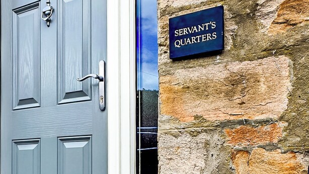 Una porta con una serratura e un cartello che indica 'SERVANT'S QUARTERS' su un muro di pietra.
