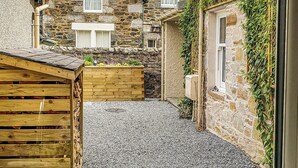 Un vialetto in pietra stretto che conduce a un edificio in pietra, con una recinzione in legno e un fioriere.