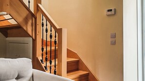 Una scala in legno con ringhiera nera, un muro bianco con termostato e un divano bianco in primo piano.
