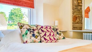Un letto rifatto con due cuscini decorati, una finestra con tenda rossa e un muro in pietra.