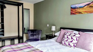 A hotel room with a bed, a chair, a nightstand, a lamp, a mirror, and a painting on the wall. - Oakbank Cottage - UK7574 (Pitlochry)