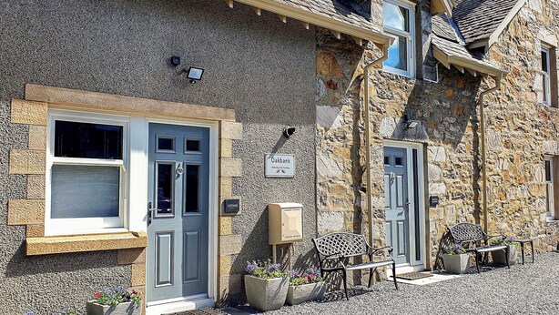 A stone cottage with a grey door, a small window, and a sign indicating it is a cottage. - Oakbank Cottage - UK7574 (Pitlochry)