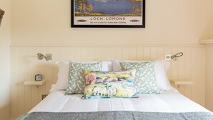 Un lit avec un oreiller coloré, un tableau encadré représentant le Loch Lomond et une tête de lit blanche.