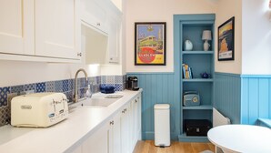 Une petite cuisine équipée d’un grille-pain DeLonghi, d’un évier, d’un radiateur et d’une petite table avec une chaise.