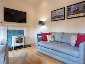 A living room with a sofa, a fireplace, a television, and two framed pictures on the wall. - 1 bedroom accommodation in Inverness (Inverness)