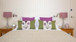 A neatly made bed with floral pillows, a bedside table with a lamp, and a clock. - Scottish Thistle - UK7561 (Inverness)