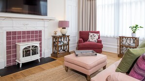 A living room with a fireplace, a television, a red armchair, and a pink ottoman. - Scottish Thistle - UK7561 (Inverness)