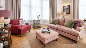A living room with a red armchair, a pink sofa, a wooden side table, and a hanging lamp. - Scottish Thistle - UK7561 (Inverness)