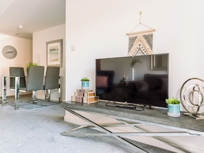 A modern living room with a flat-screen TV, two grey chairs, a small table with a plant, and a decorative wall hanging. - 2 bedroom accommodation in York (York)