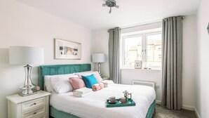 Un dormitorio ordenado con cama, mesitas de noche, una ventana con cortinas e imagen enmarcada en la pared.