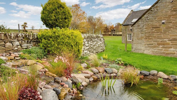 A stone building with a small pond, surrounded by a stone wall and various plants. - 3 bedroom accommodation in Forfar (Forfar)