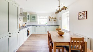 A modern kitchen with light green cabinets, a wooden dining table with chairs, and a pendant light fixture. - 3 bedroom accommodation in Forfar (Forfar)