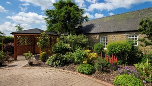 A stone house with a wooden gazebo, surrounded by a garden with various plants and flowers. - 3 bedroom accommodation in Forfar (Forfar)