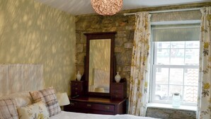 Een slaapkamer met een groot bed, een dressoir, een spiegel en een raam met gordijnen.