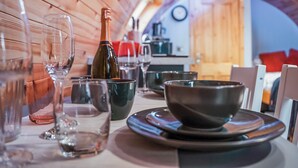 Una mesa de comedor preparada con copas de vino, una botella y cuencos en un ambiente de madera.