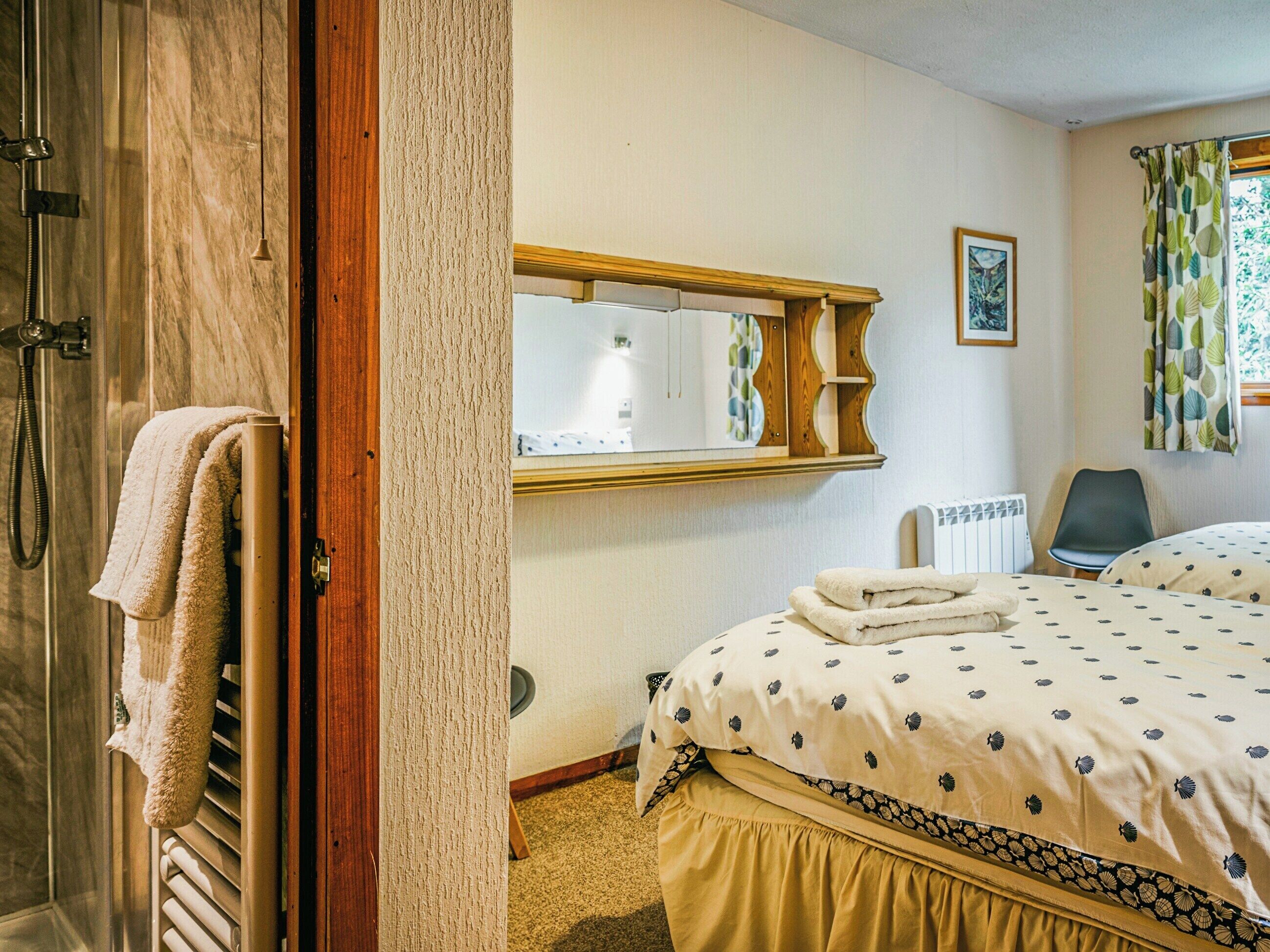 A hotel room with a bed, a chair, a radiator, a shower, and a mirror.