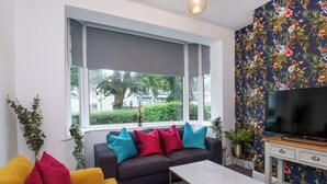 Un salon comprenant un canapé, une table basse, un téléviseur et une fenêtre avec des stores.