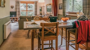 A cozy living room with a sofa, dining table, and chairs. There is a television, a lamp, and a window with curtains. - We love this hidden little secret. (Moffat)
