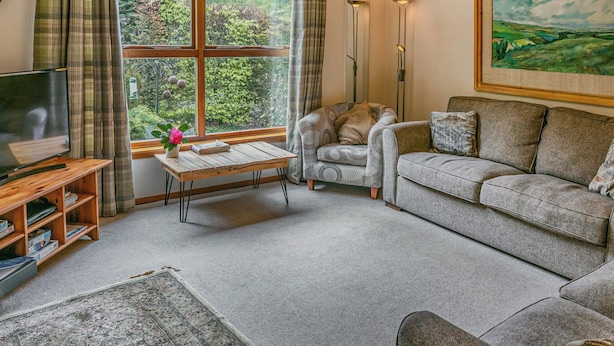 A cozy living room with a large window, a television, a patterned armchair, a sofa, and a painting on the wall. - We love this hidden little secret. (Moffat)