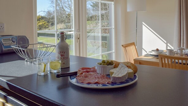 Een ontbijttafel met een bord kaas, olijven en brood, een fles wijn en een radio.