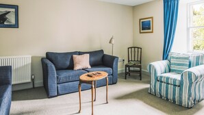 A living room with a blue sofa, a striped armchair, a small wooden table, and a radiator. - Clachan Annex - UK7626 (Pitlochry)