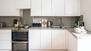 A modern kitchen with white cabinets, a built-in oven, a sink, and various kitchen appliances. - Clachan Annex - UK7626 (Pitlochry)