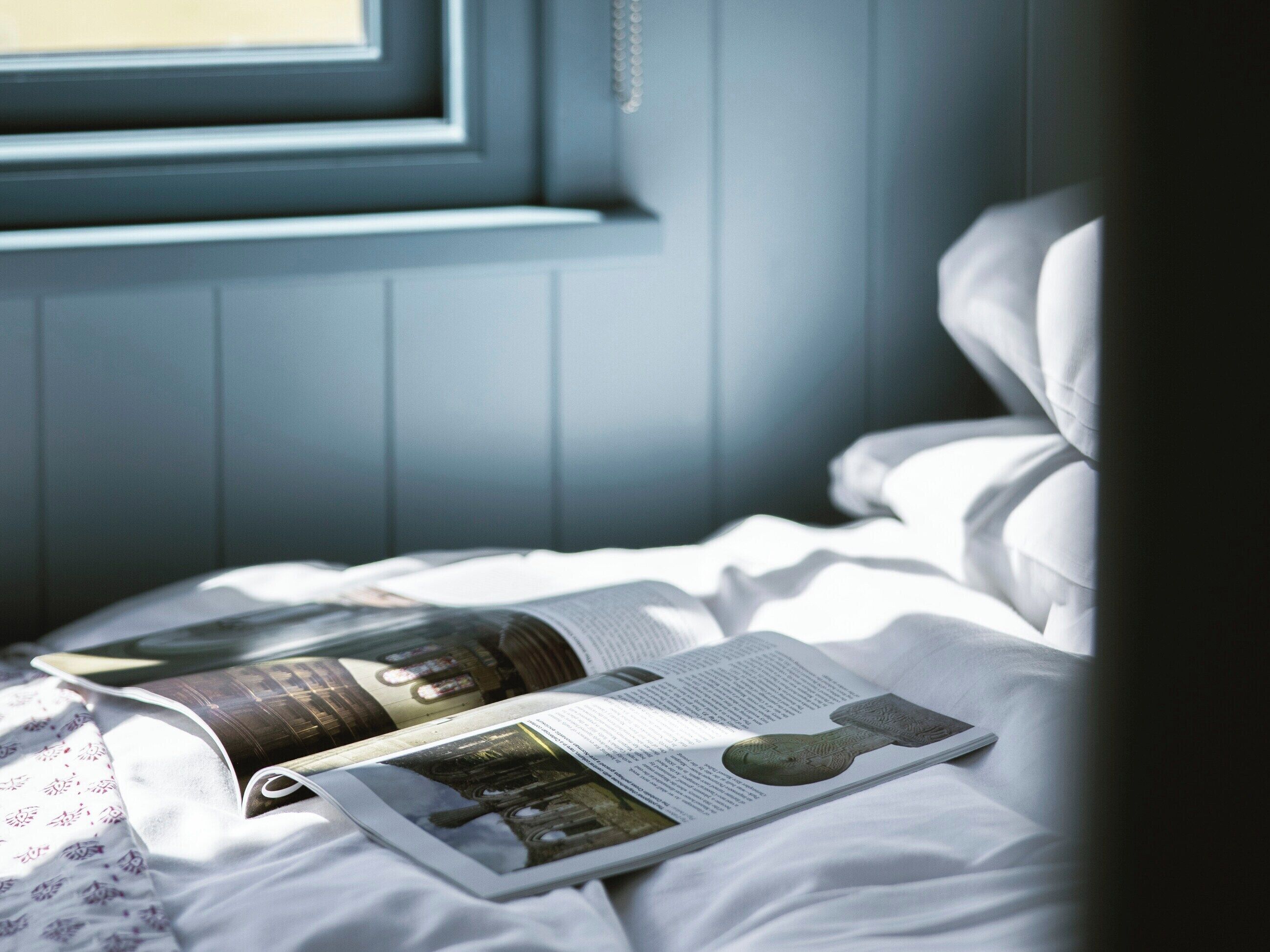 A bed with a magazine open, a window, and a door.