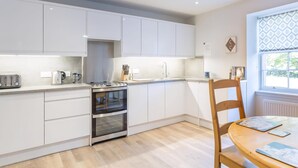 Eine moderne Küche mit weißen Schränken, einem eingebauten Backofen, einem Wasserkocher und einem Essbereich mit einem Holztisch und Stühlen.