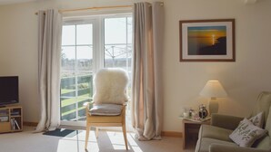 A living room with a large window, a fluffy chair, a green sofa, a lamp, and a framed picture on the wall. - Willow Cottage - UK30684 (Sandhead)