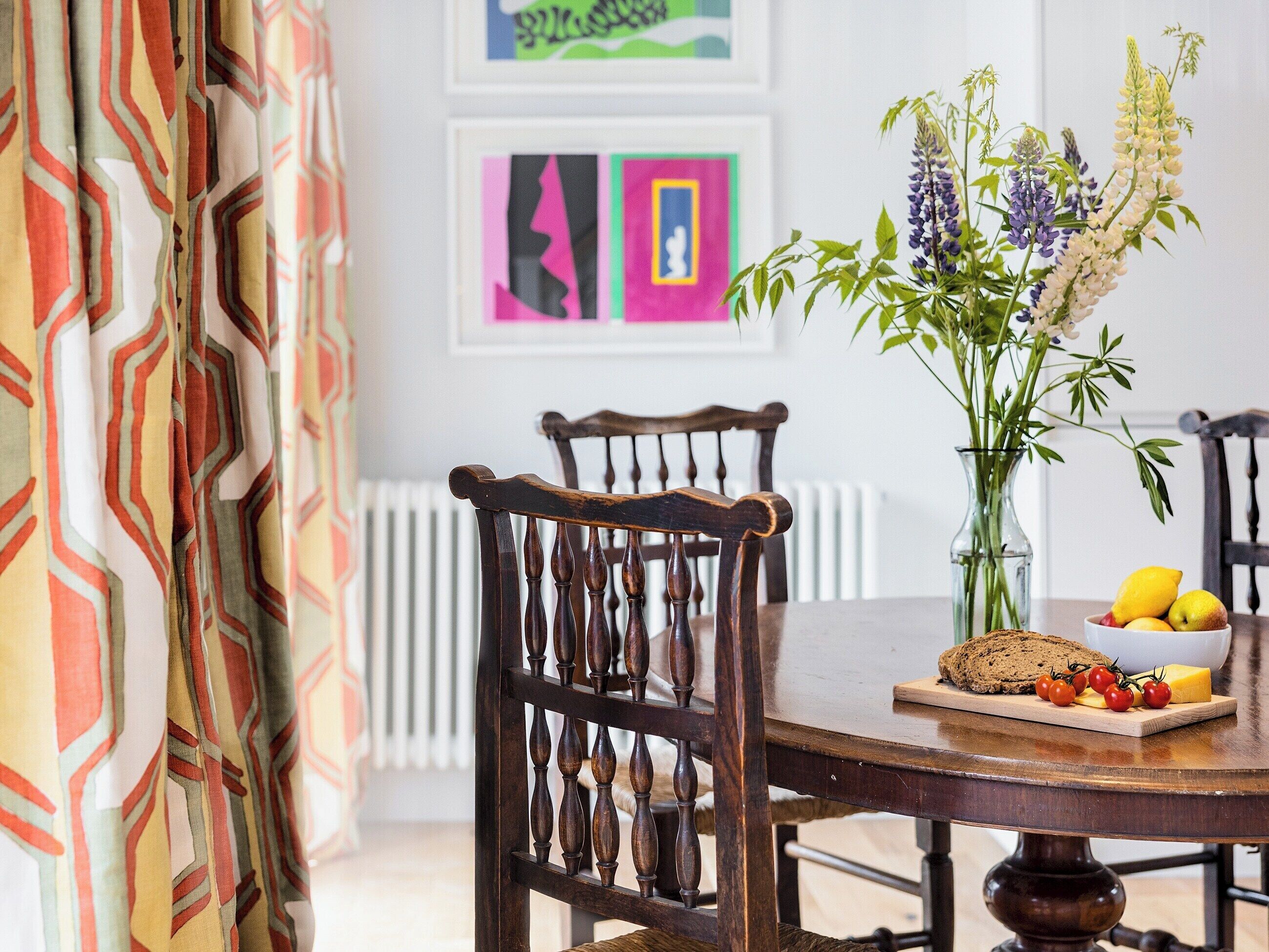 Een eetgedeelte met een houten tafel, stoelen, een vaas met bloemen en een bord met eten.