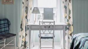 Quarto com escrivaninha, cadeira, luminária e janela com cortinas.