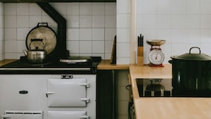 A kitchen with a stove, kettle, scale, and utensils.