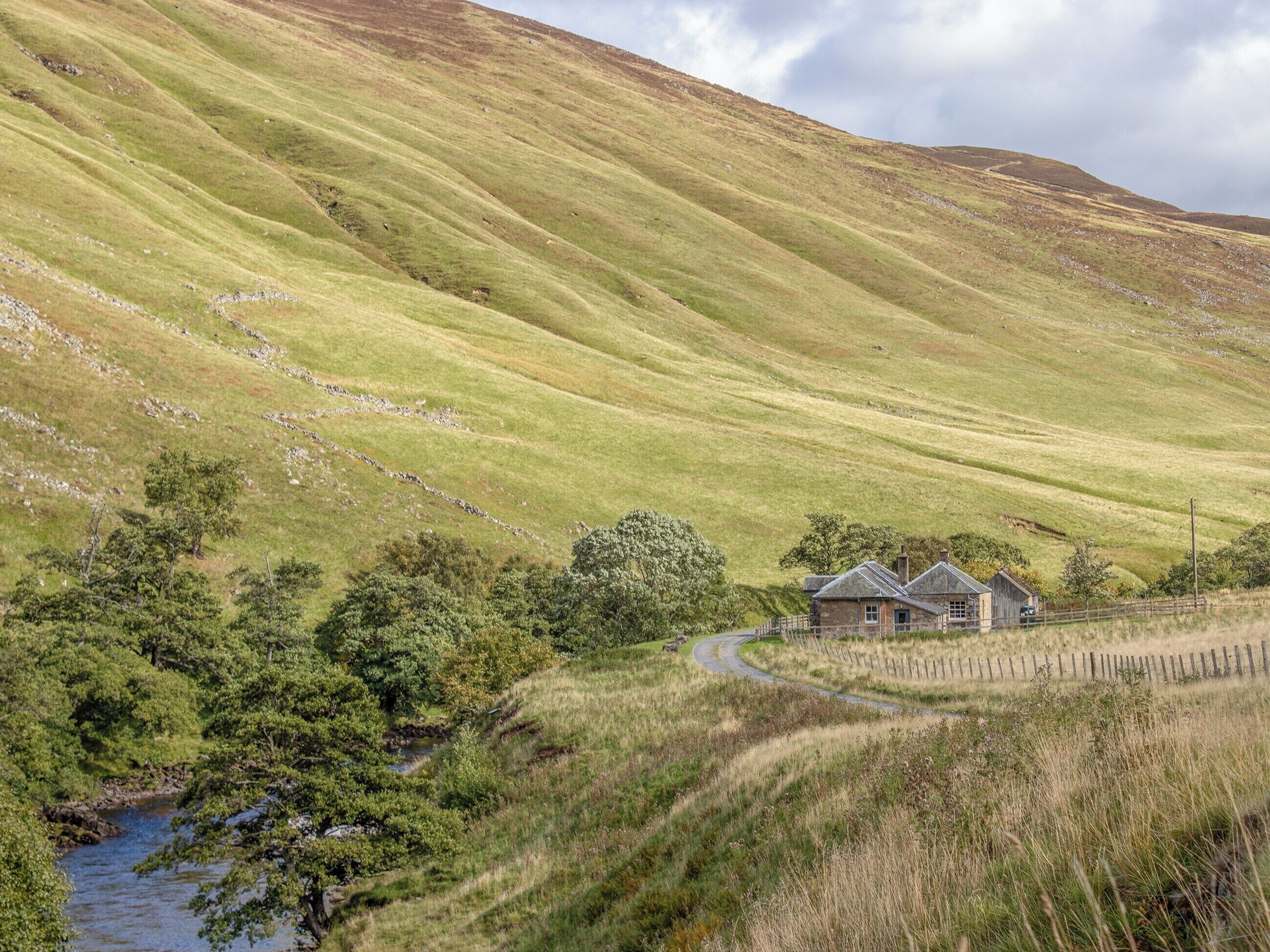A rural landscape with a stone house, a winding road, and a stream.