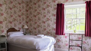 A bedroom with floral wallpaper, a bed with white linens, a nightstand with a lamp, and a window with curtains. - Marble Lodge - UK7635 (Pitlochry)