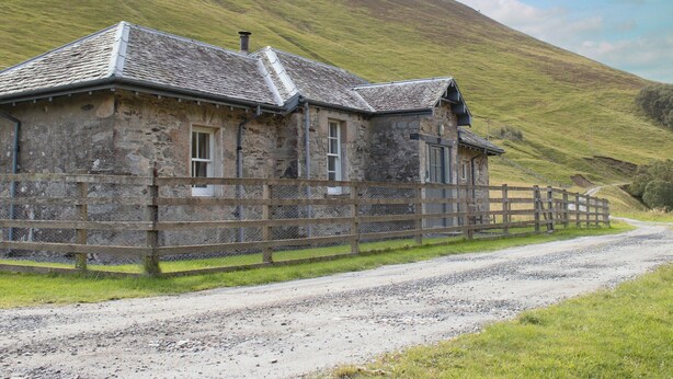 A stone building with a sloped roof, a wooden fence, and a gravel road. - Marble Lodge - UK7635 (Pitlochry)