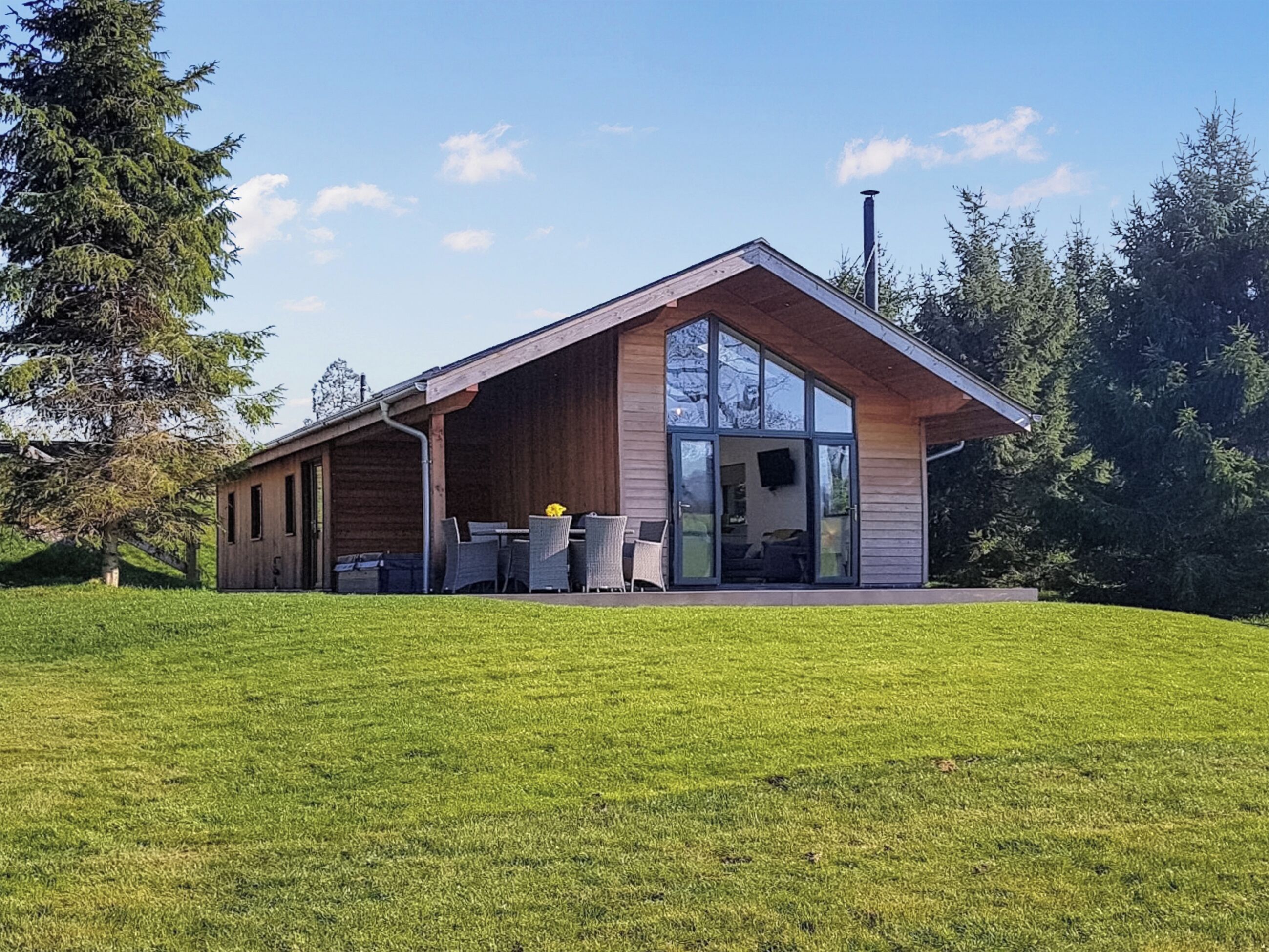 Une maison moderne dotée d’une grande porte vitrée, d’un patio couvert et d’une pelouse verdoyante.