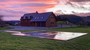 Una casa de madera con techo inclinado, un camino de entrada y un área verde con superficie reflectante.
