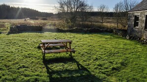 Una mesa de picnic en un campo cubierto de hierba, con un muro de piedra y un edificio de piedra al fondo.