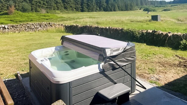 A hot tub in an outdoor setting with a stone wall and a grassy field in the background. - Merrick Cottage - UK7783 (Newton Stewart)