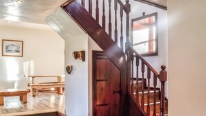 A wooden staircase with a handrail, a wooden door, and a bench in a room with light-colored walls and wooden flooring. - Merrick Cottage - UK7783 (Newton Stewart)