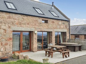A stone building with large glass doors, a wooden picnic table, and a barbecue area. - The Stables - UK7791 (Lumphanan, near Banchory)