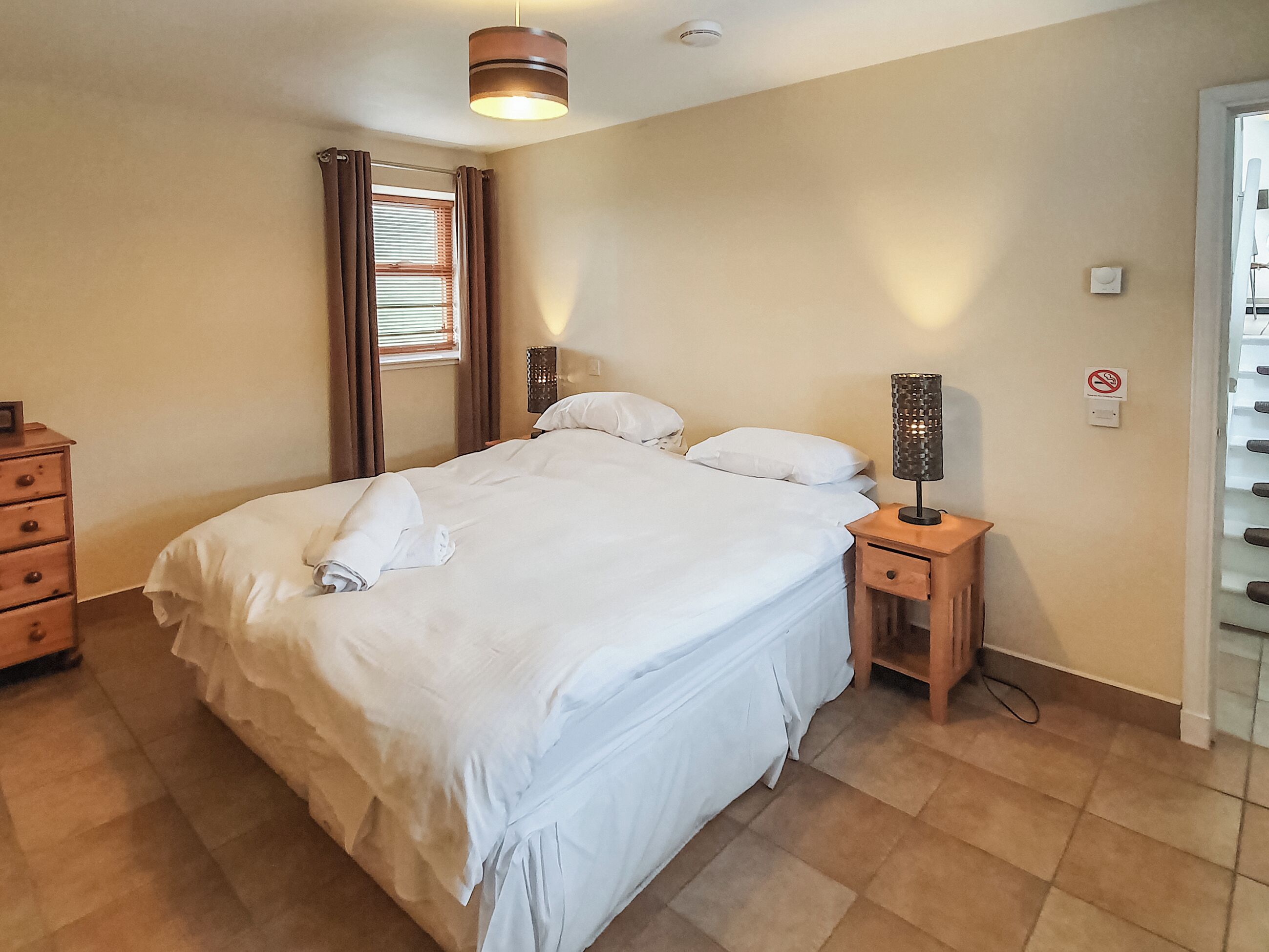 A neatly made bed with white linens, a bedside table with a lamp, and a dresser.