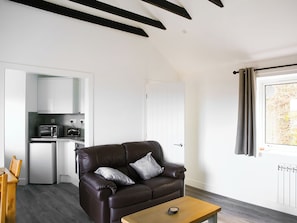 A modern living room with a brown leather sofa, a wooden coffee table, and a kitchen area with a microwave and a small refrigerator. - This house was built for two to enjoy. (Portuairk)