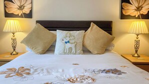 Una cama con colcha estampada, dos lámparas de pared y tres almohadones decorativos.