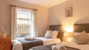Quarto de hotel com duas camas, uma cômoda de madeira, janela com cortinas, luminária e um quadro na parede.