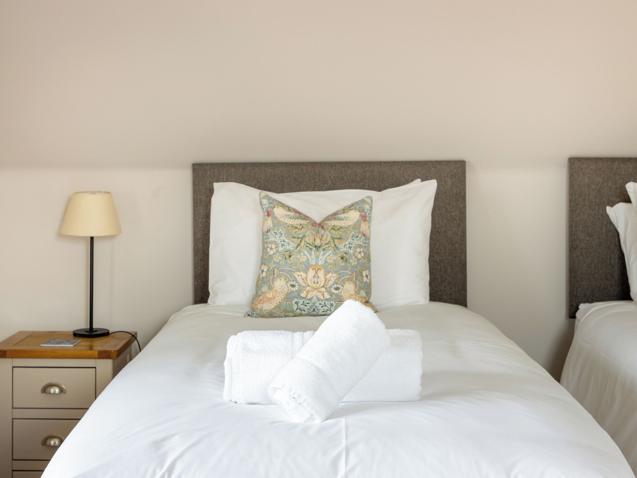 A neatly made bed with white linens, a floral pillow, and a folded towel on the bed.