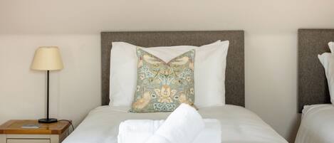 A neatly made bed with white linens, a floral pillow, and a folded towel on the bed.