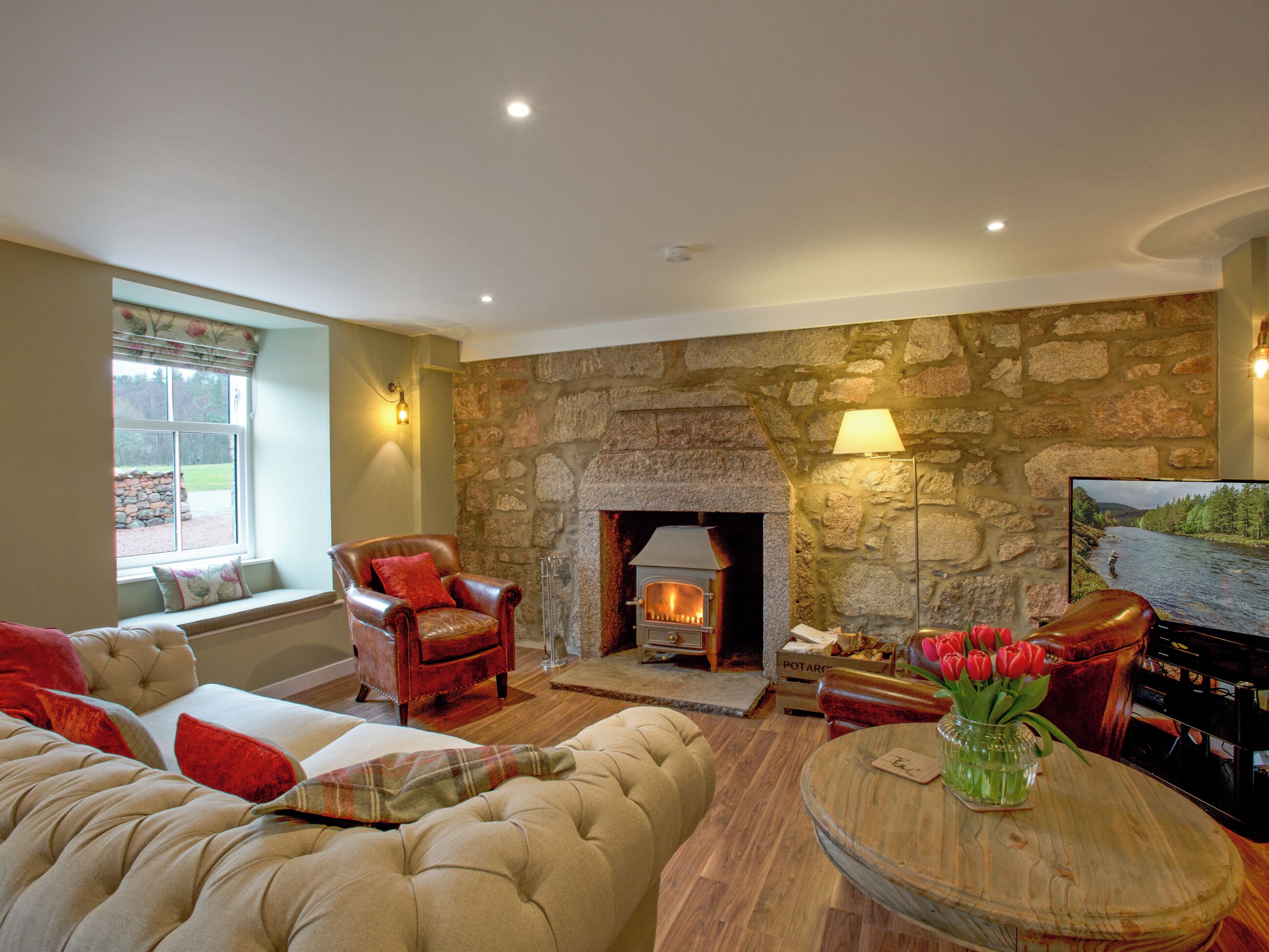 A cozy living room with a stone fireplace, comfortable seating, and a television.