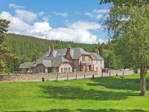A stone building with multiple chimneys, a stone wall, and a grassy area with benches. - 7 bedroom accommodation in Potarch, near Banchory (Potarch, near Banchory)
