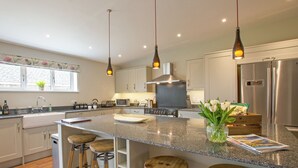 Una cocina moderna con encimeras de granito, electrodomésticos de acero inoxidable, taburetes de madera e iluminación colgante.
